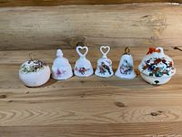 Front view of six decorative bells in a row on wooden surface showing detailed floral and bird patterns on porcelain and ceramic materials.