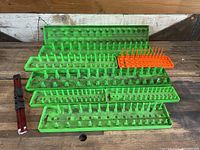 Multiple bright green plastic socket trays and one orange Snap-On socket organizer tray, arranged on wooden surface, with a red aluminum rail visible