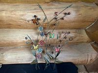 Full view of metal floral wall sculpture featuring flowers and colorful butterflies and dragonflies against a wood background