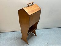 Full view of mid-century wooden sewing cabinet with angled legs and closed hinged lid showing the built-in wooden handle at the top.