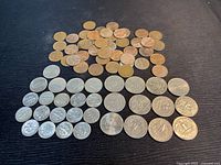Coins laid out on dark surface showing four rows with pennies, nickels, dimes, and quarters.