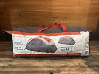 Photo of the soft carry bag containing the outbound 8-person dome tent, showing the printed label with images and specs.