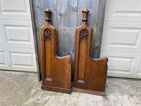 Pair of antique oak church pew ends shown front side, standing outdoors against wooden gate