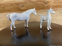 Photo of the pair of Beswick porcelain horse figurines displayed on a black surface against a wood background, showing the side profile of both the mare and foal.