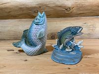 Two vintage cast iron hand-painted fish doorstops on a wooden surface with log background.