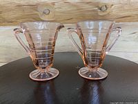 Pair of pink Depression glass creamer and sugar bowl displayed side by side on a dark round table against wood background.