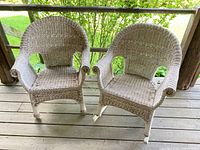 Front view of two white wicker chairs on wooden floor; one rocker, one armchair.