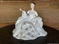 Front view of the Royal Doulton figurine showing the seated lady holding a pink rose with a white dress decorated with gold floral accents.