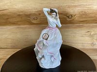 Front angle showing the figurine in a flowing white gown trimmed with pink, holding her bonnet.