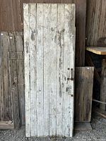 Front view of vintage barn door with weathered white paint and wooden handle, showing surface wear and chipping paint.