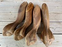 Four carved wooden furniture legs with claw/paw feet placed on a wooden floor, showing the natural wood grain and carved details.