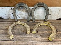 Four vintage cast iron horseshoes displayed on wooden surface with two raw iron horseshoes at back and two yellow painted horseshoes in front.