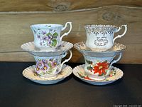 Four stacked bone china teacups on matching saucers, each cup featuring different floral designs and gold rims.
