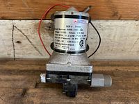 Front view showing detailed product label with model number, voltage (12V DC), amperage (7.5 max), flow GPM (3.0), shut-off pressure (55 PSI), and fuse rating (10 AMP).