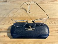 Front view of vintage rimless gold-filled eyeglasses displayed on original hard shell case with embossed branding.