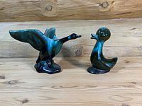 View of two Blue Mountain Pottery figurines including standing duck and flying goose on wooden background.