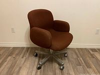 Left side angle view of vintage brown fabric office chair on five-star steel base with casters, showing molded seat and integrated arms.