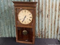 Full view of vintage wooden framed wall clock with glass front panels, visible pendulum and classic mechanical design.