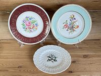 Three vintage English floral plates displayed on wooden surface, arranged side by side with visible floral designs and borders.