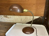 Side view of vintage brown enameled gooseneck desk lamp on wooden surface, showing dome shade and weighted base.
