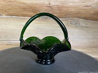 Front view of the vintage green pressed glass basket showing the ruffled rim, scrolled design, and clear glass handle.