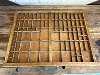 Top view of wooden printer's type tray showing multiple compartments and metal label plate on front.