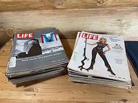 Two stacks of vintage LIFE magazines from the 1960s displayed on a wood surface, covers show varied themes and eras.