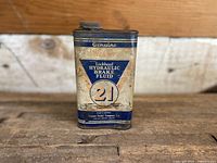 Front view of vintage Lockheed Hydraulic Brake Fluid Tin. Rectangular metal container with blue and white label and screw-on metal cap. Shows signs of wear and age.