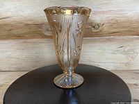 Front view of the marigold carnival glass vase showing the floral iris motif, vertical ribbing, scalloped rim, and pedestal base.