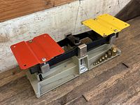 Front perspective of the Ohaus mechanical dual-pan balance scale showing red and yellow metal trays, black beam, and gray base with Ohaus badge.