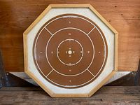 Full view of the crokinole side of the vintage octagonal wooden game board, showing scoring rings and central 20 hole, with wooden frame.