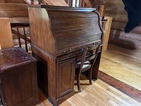 Front three-quarter view of desk with roll-top closed and chair at right