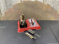 Photo showing the vintage Wilesco style stationary toy steam engine on red metal base with brass boiler, vertical chimney, red flywheel, and two spirit burners positioned beside the engine.