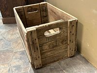 Side angled view showing the crate's cut-out handle, weathered wooden slats, and faint stamped markings on the inside and outside.