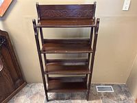 Front view of wooden four-tier shelf with carved floral top backboard, showing full piece and dark wood finish.