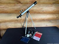 Overview photo showing telescope on tripod with accessories including binoculars, coin book, jar, letter opener, flag, and umbrella.