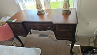 Front view of antique wooden desk showing top surface, drawers, and legs with carvings and curved lines.