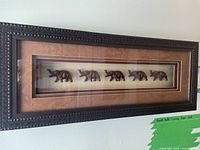 Full view of the wood framed shadow box mounted on a wall, showing five carved wood elephants inside.