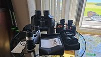 Four pairs of binoculars arranged on a glass table near window showing different sizes and types.