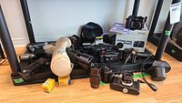 Full lot overview showing cameras, lenses, flash, camera bags, film canisters, and other accessories arranged on floor.