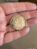 Close-up of a 1962 Canadian 50 cent coin showing the Canadian coat of arms on the reverse side, held in hand.