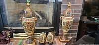 Photo showing two large cloisonne lidded urns and two smaller ceramic eggs arranged side by side in front of fireplace.
