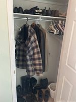Closet interior showing men’s clothing hanging, shoes and boots size 9 on the floor, and several hangers on the rod.