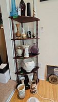 Dark wood corner display cabinet with five shelves, holding various vases and decorative items for photo only. Cabinet dimensions approximately 21x15x52 inches, curved front edges to fit in corner. No glass panels.
