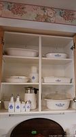 Full view of cupboard with Corningware Blue Cornflower collection of casserole dishes, serving plate, coffee percolator, milk jar and glass shakers