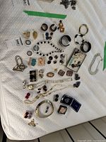 Overview of various jewelry items spread out on a white textured surface including earrings, necklaces, brooches, and bangles.