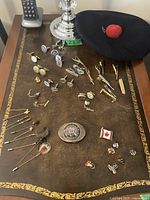 Overview of various cufflinks, tie clips, pins, belt buckle and curling tam laid out on a leather surface with a cordless phone in background.