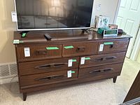 Seven-drawer dresser in dark mid-century wood finish with TV on top, showing front view with drawer design and handles.