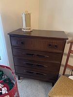 Overall dresser with four drawers and a decorative item on top, showing the dark wood finish and straight lines of the piece.