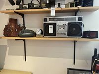 Shelf showing multiple items including the Telefunken boom box in the center with labels, clocks to left and right.